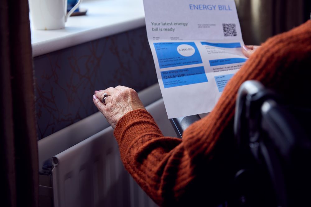 Close Up Of Senior Woman In Wheelchair With Energy Bill By Radiator